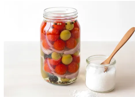 Encurtido en botella de tomates, cebolla y aceitunas con un frasco de sal al lado
